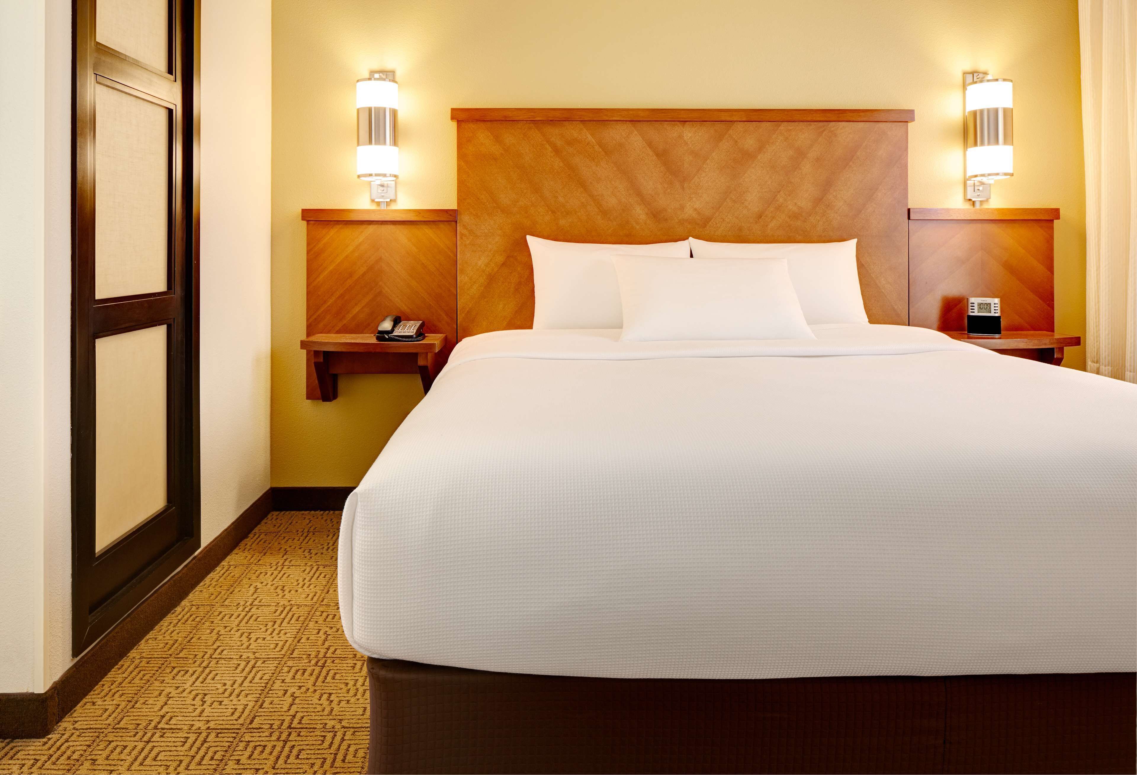 A hotel room with a large bed, two bedside tables, a wooden headboard, and wall-mounted lights.