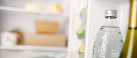 Una botella transparente de agua en un refrigerador con estantes que contienen diversos alimentos y recipientes.