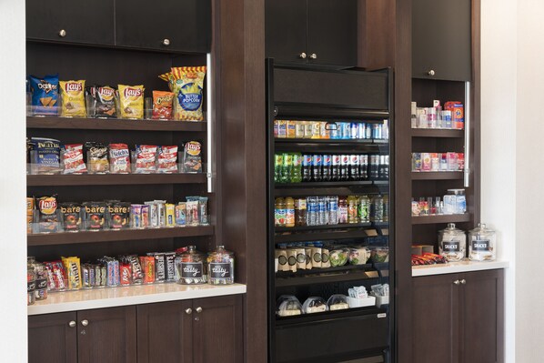 A snack and beverage vending machine in a hotel lobby, surrounded by shelves stocked with various snacks and beverages.