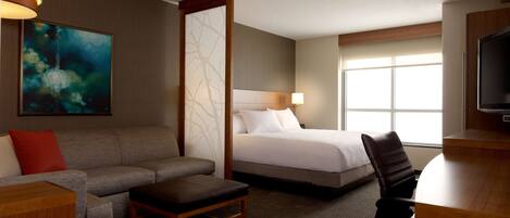 A hotel room with a bed, a sofa, a desk, a chair, a TV, and a window.