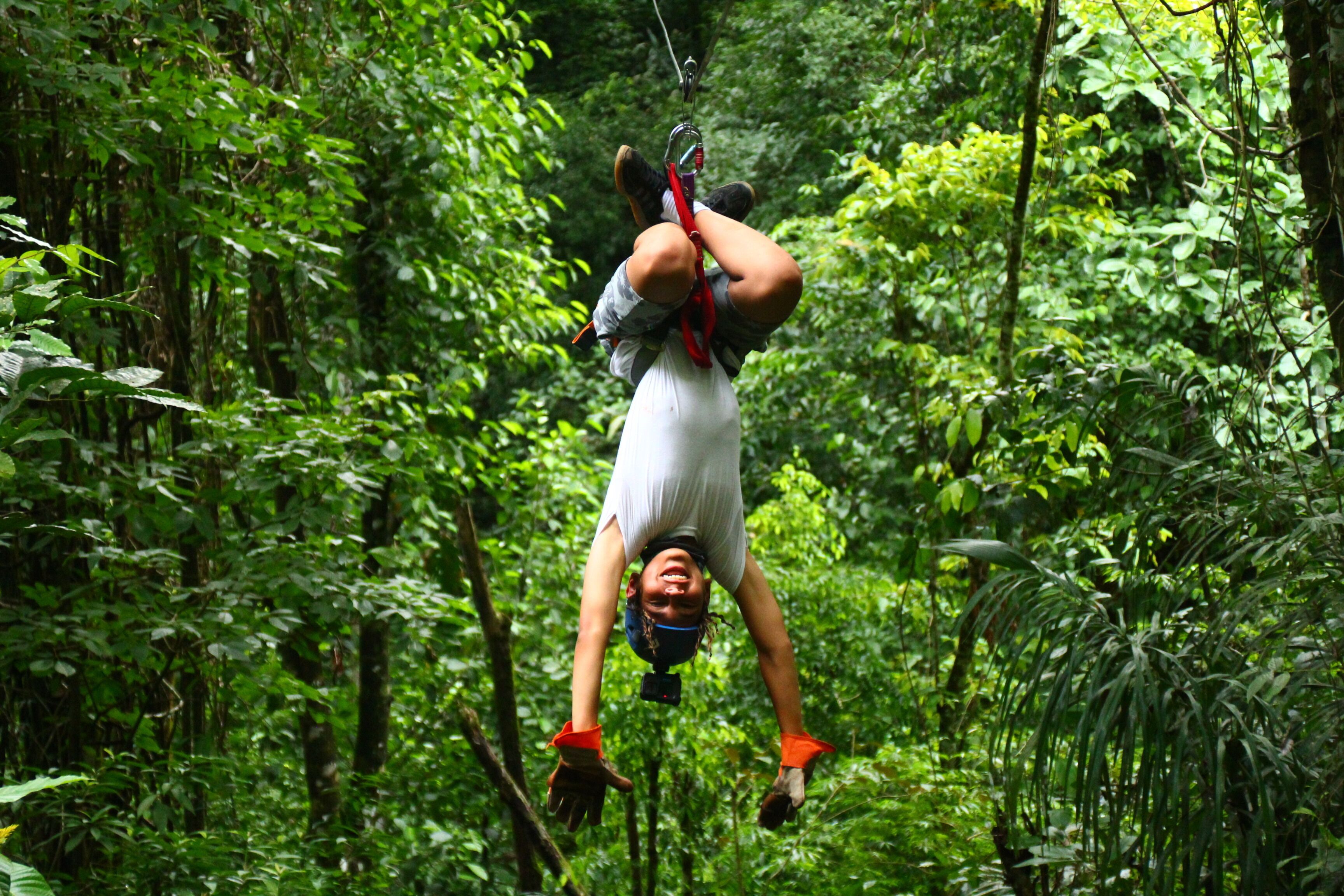 A person suspended in a forest, wearing a harness and helmet, with a rope attached to a tree.