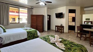 Una camera d'albergo con due letti, una ventola a soffitto, una televisione, una scrivania e un'area pranzo.