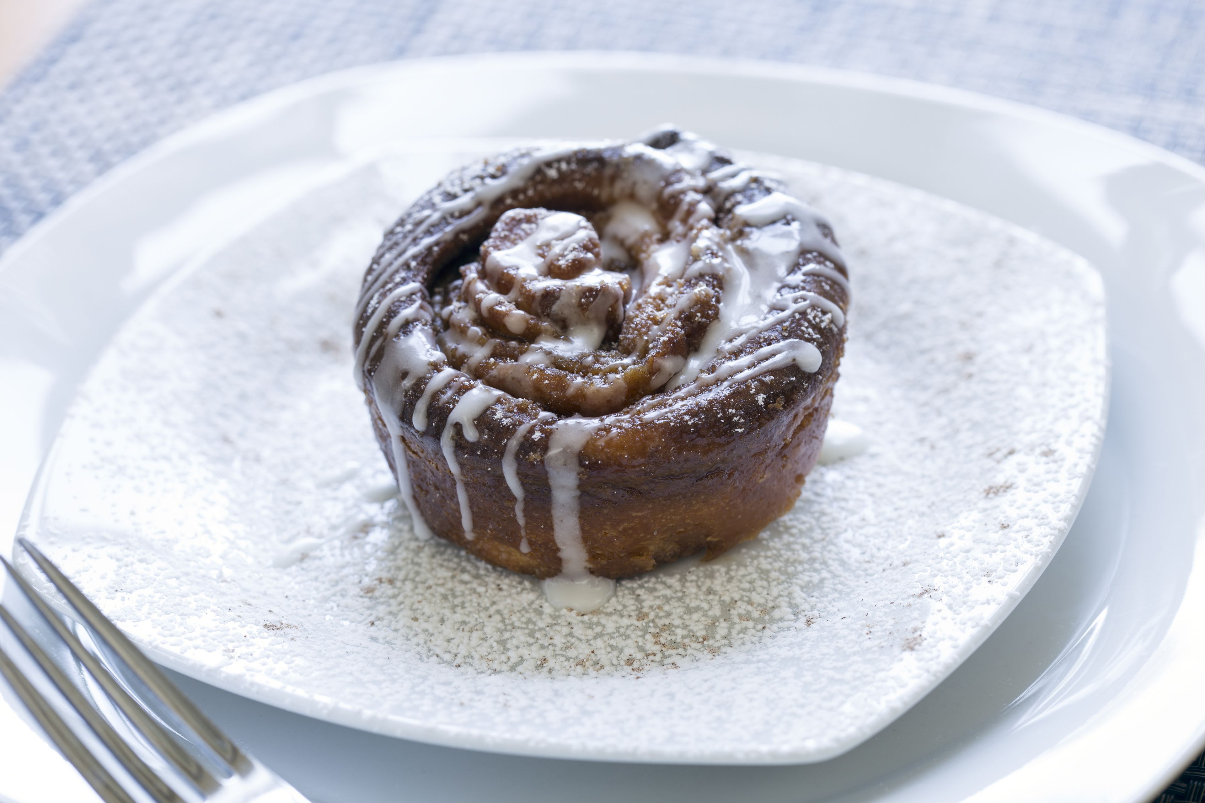 Un pain aux cannelle sur une assiette blanche, saupoudré de sucre glace.