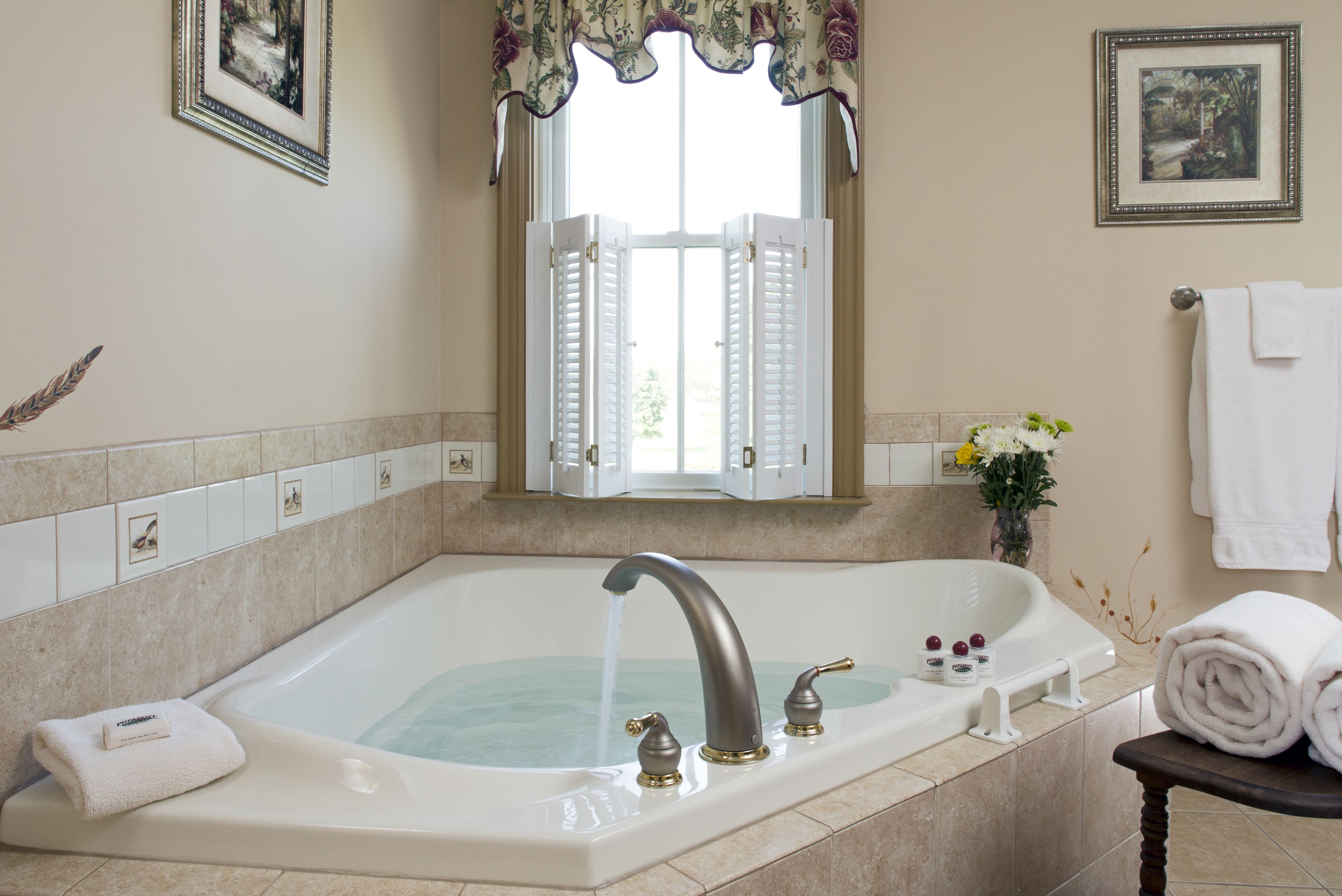 A bathroom with a large bathtub, a window with shutters, and a towel rack.