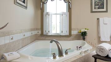 A bathroom with a large bathtub, a window with shutters, and a towel rack.