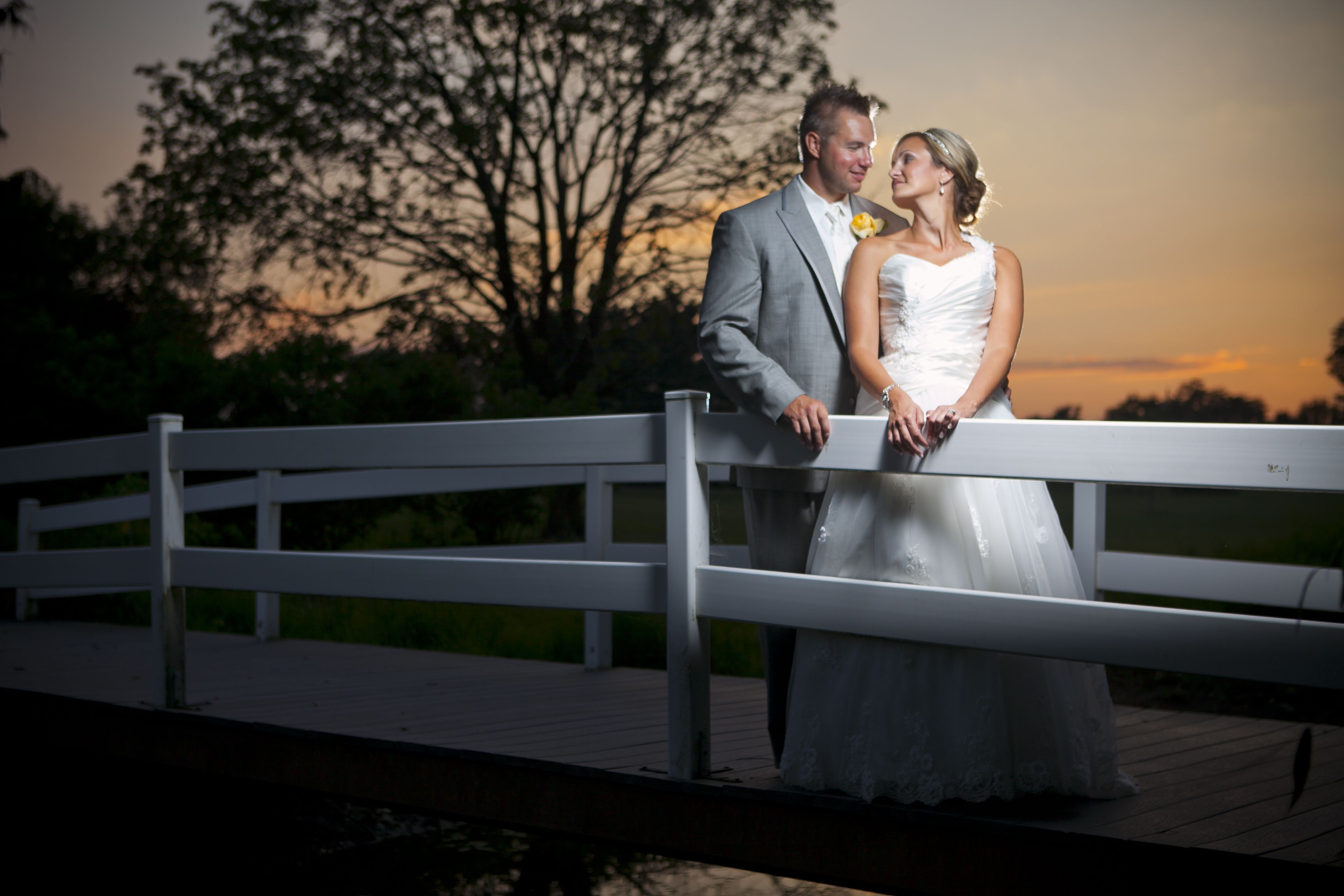 Una pareja en un puente de madera con un atardecer de fondo.