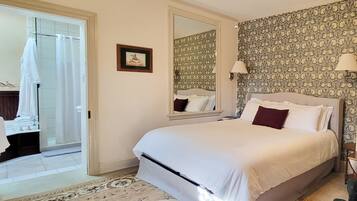 A bedroom with a large bed, a mirror, patterned wallpaper, and a door leading to a bathroom.