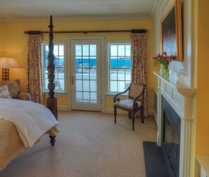 A hotel room with a bed, a chair, a fireplace, and a view of the sea through the door. - The Inn at Stonington (Stonington)