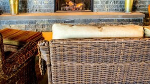 A stone fireplace with a fire, wicker furniture, and decorative plants. - The Inn at Stonington (Stonington)
