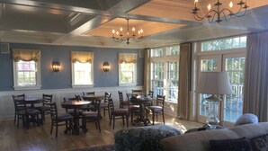 A dining area with wooden tables and chairs, a chandelier, and large windows with curtains. - The Inn at Stonington (Stonington)