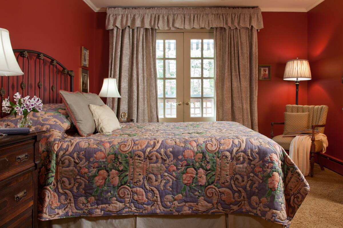 A bedroom with a floral bedspread, a dresser, a chair, and a lamp.