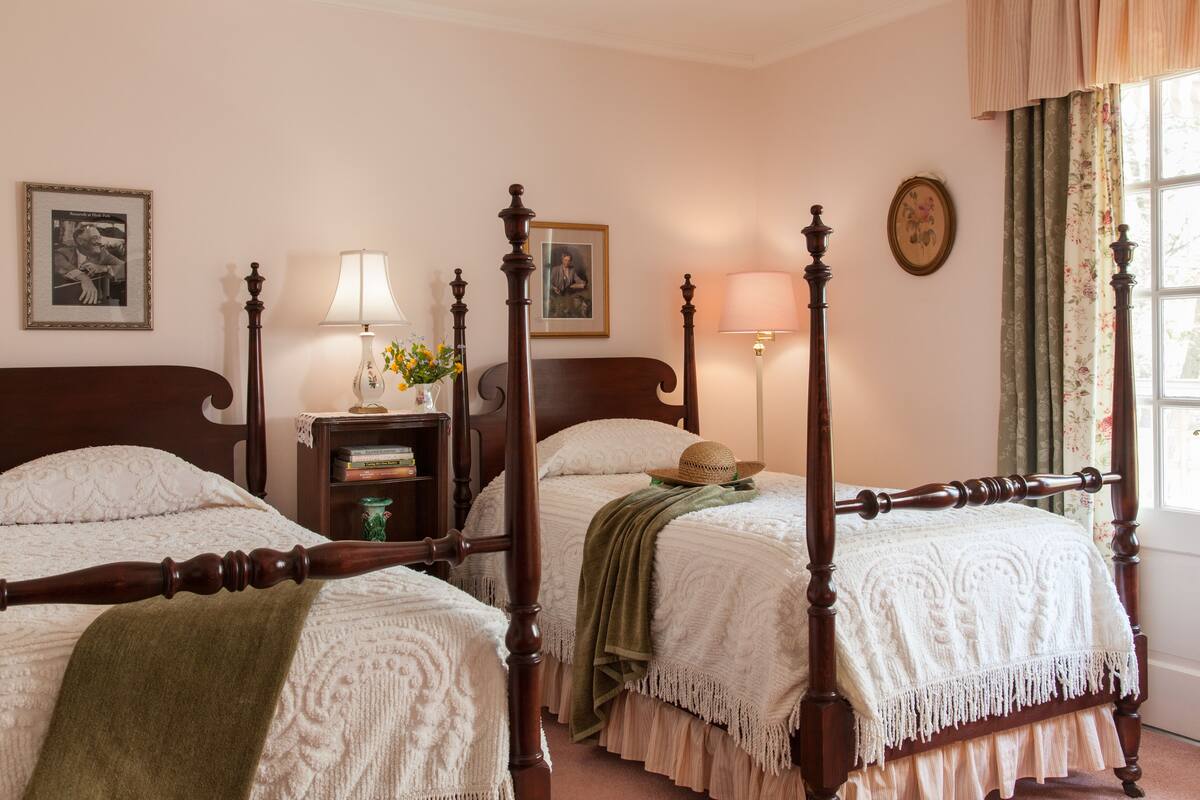 A four-poster bed with a green throw blanket, a bedside table with a lamp, and a vase with flowers.