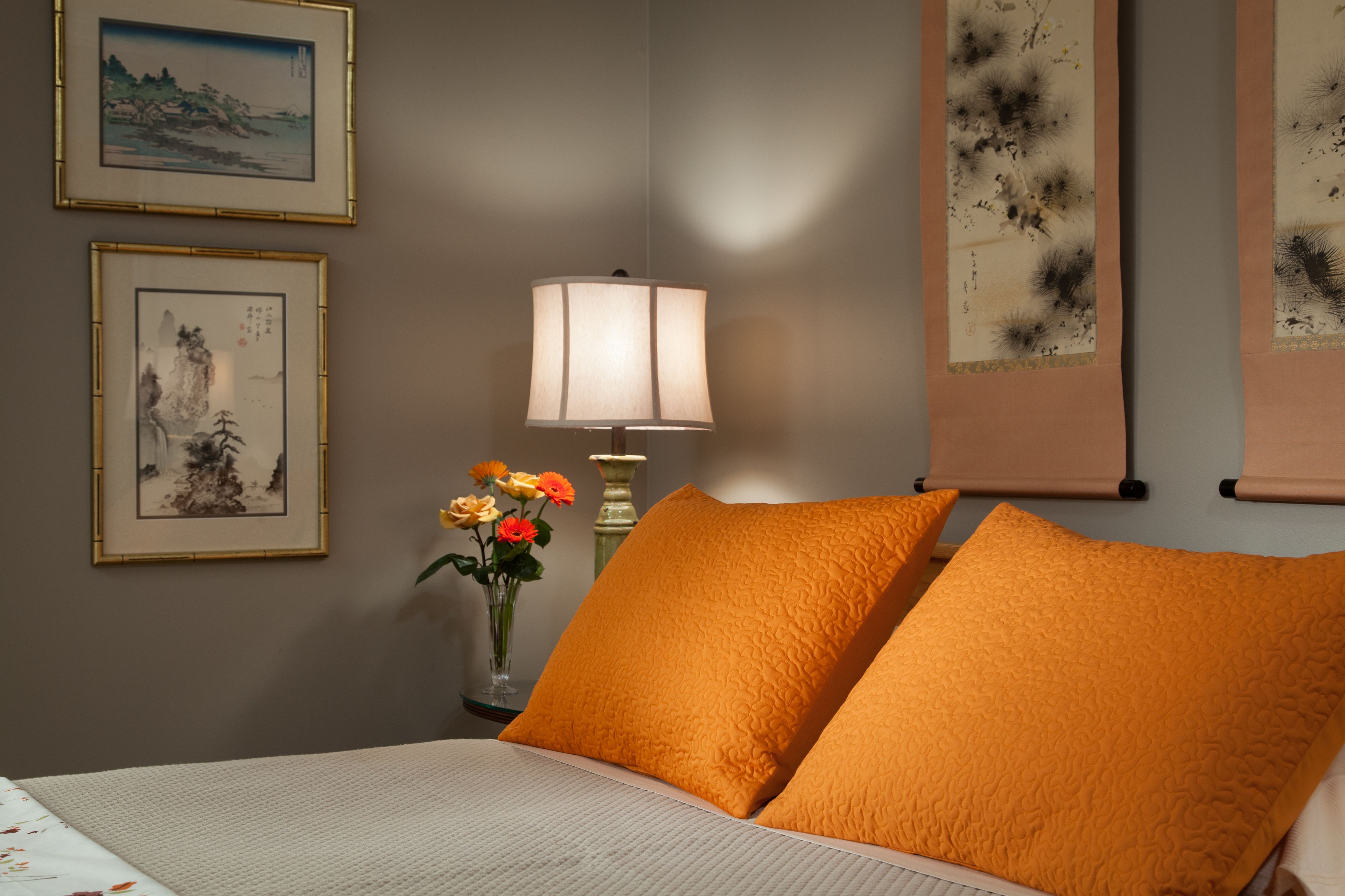 Un dormitorio ordenado con cama, almohadas, una lámpara y cuadros en la pared.