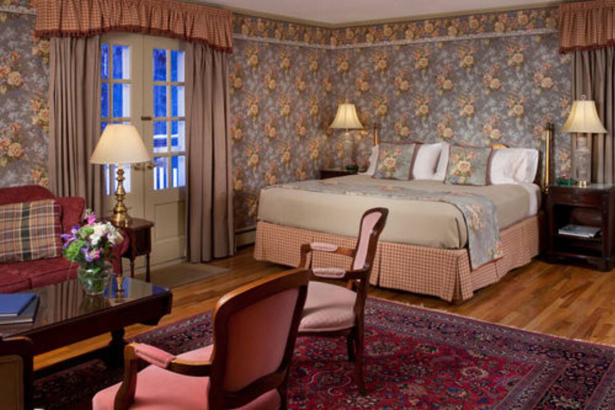 A bedroom with a bed, two bedside tables, a chair, a desk, and a window with curtains.