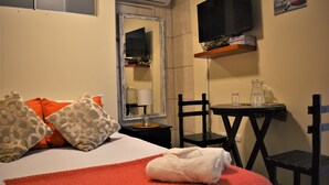 Une chambre d’hôtel avec un lit, un téléviseur fixé au mur, une petite table et une chaise.