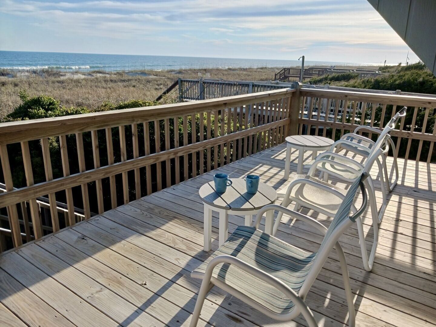 A wooden deck with a railing, two tables, and four chairs.