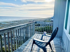Eine Holzterrasse mit Stuhl und Tasse, mit Blick auf Strand und Meer.