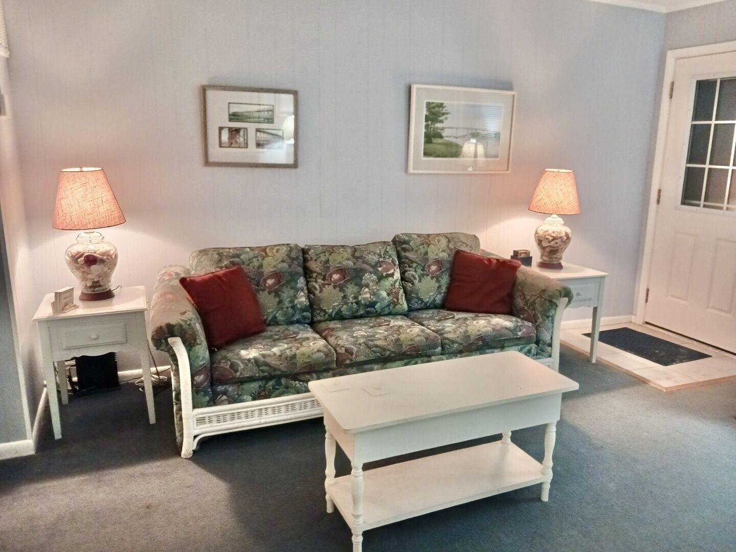 A living room with a floral sofa, two side tables with lamps, a white coffee table, and two framed pictures on the wall.