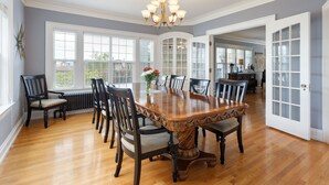 A dining room with a large wooden table surrounded by chairs, a chandelier, and large windows with blinds. - Nantucket Inn (Anacortes)