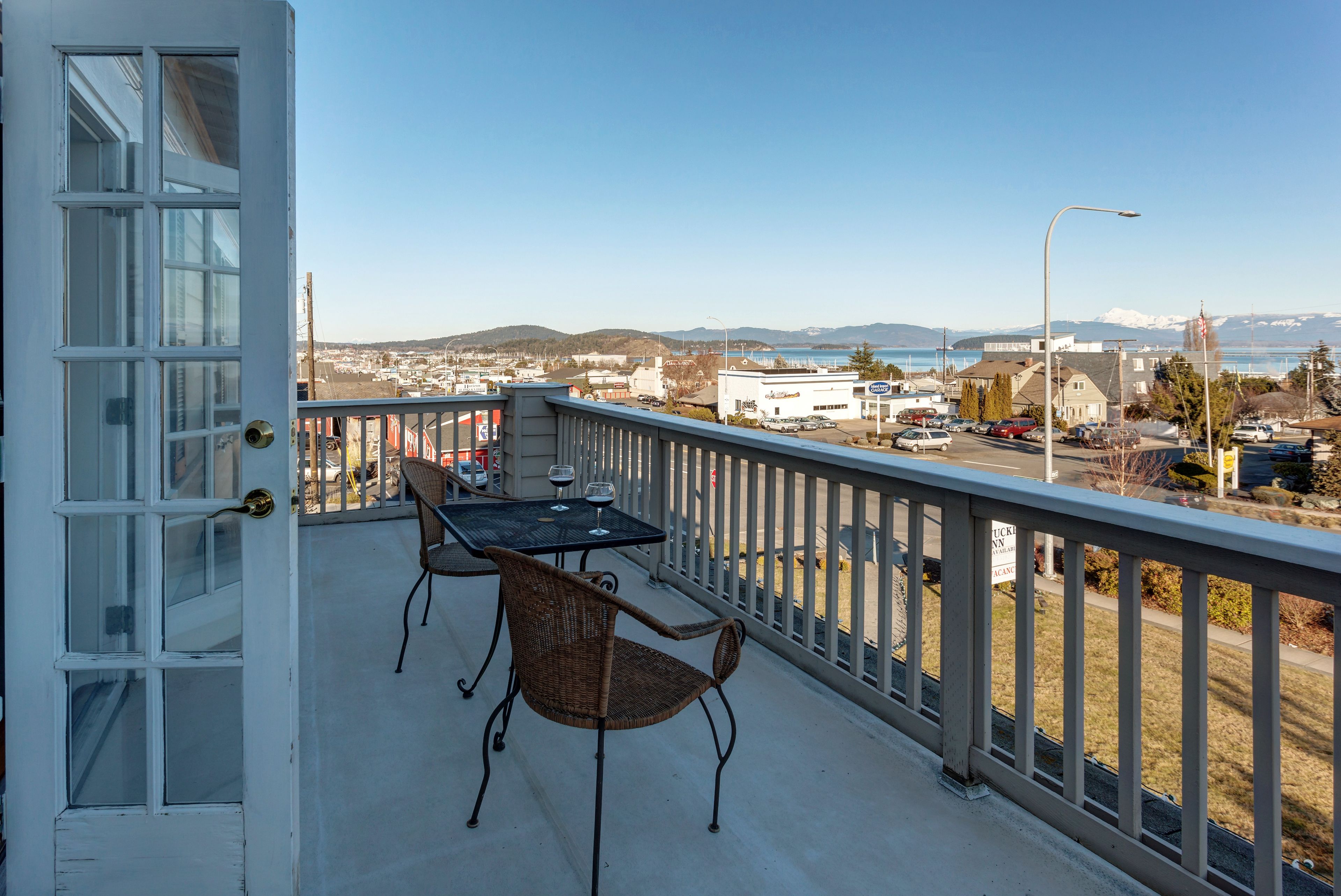 A balcony with a table and chairs, overlooking a town and mountains.