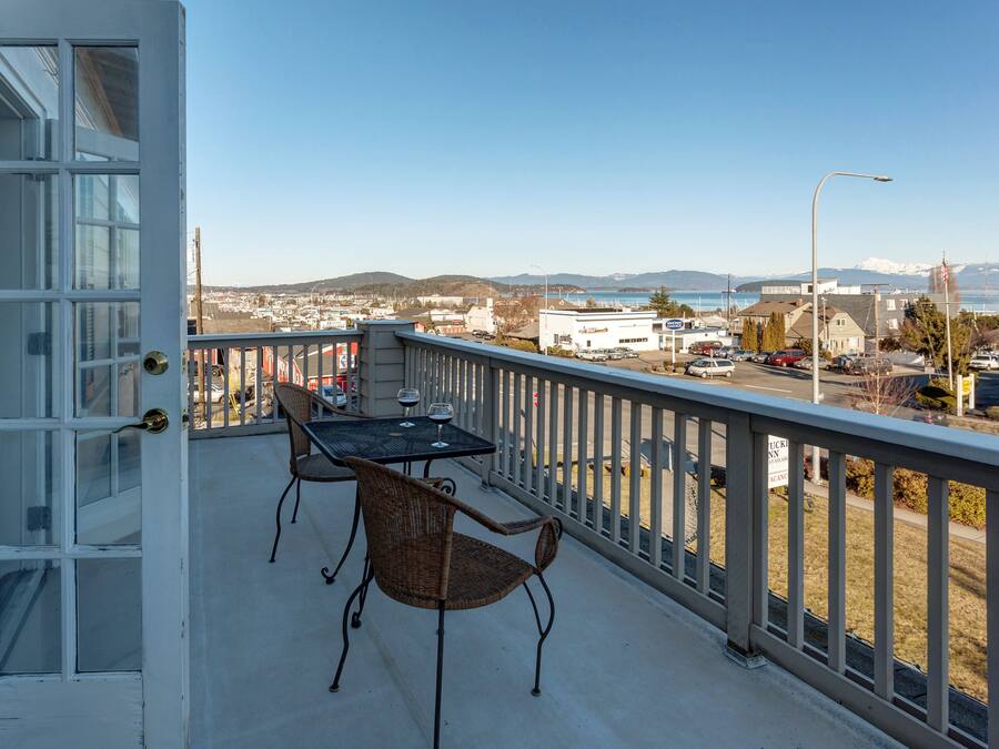 A balcony with a table and chairs, overlooking a town and mountains.