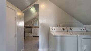 A laundry room with two front-loading washers and dryers, a white door, and a hallway leading to a bathroom with a vanity and cabinets.