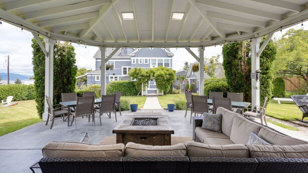 A covered patio with a fire pit, outdoor furniture, and a view of a house in the background. - Nantucket Inn (Anacortes)