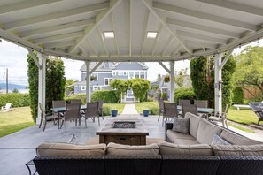 A covered patio with a fire pit, outdoor furniture, and a view of a house in the background. - Nantucket Inn (Anacortes)