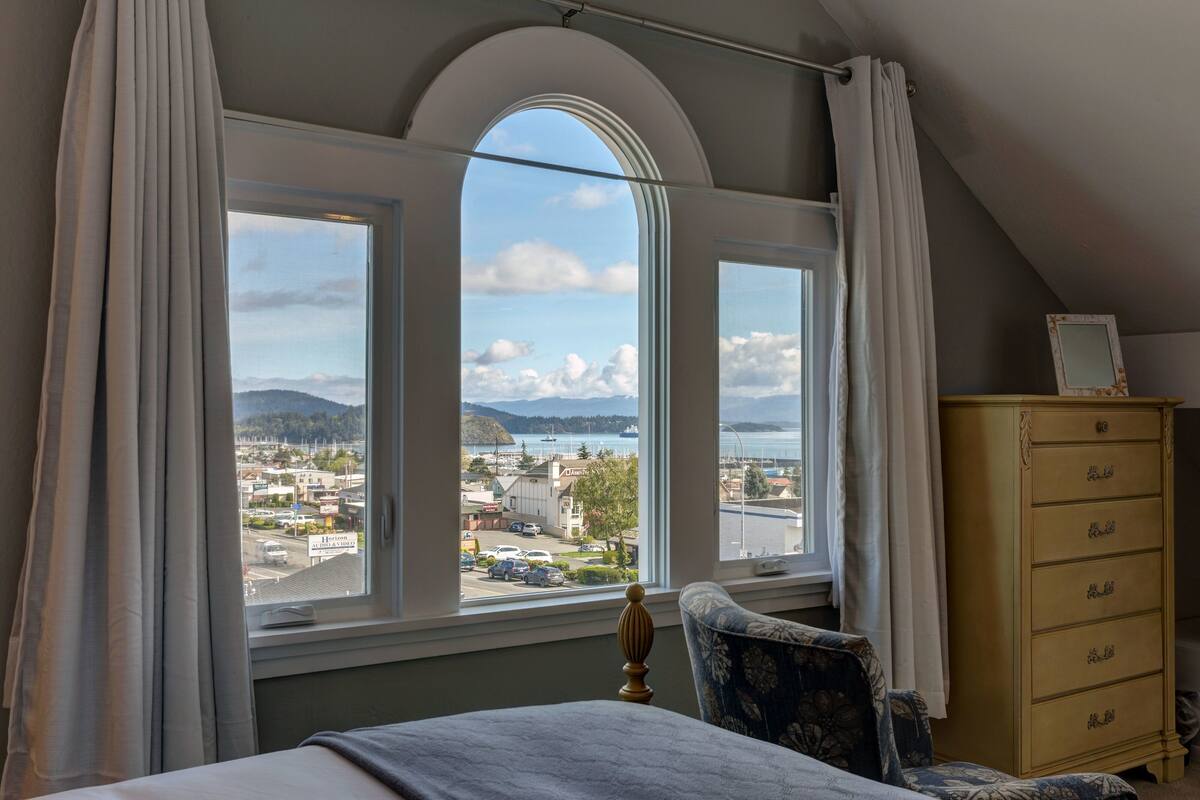 A bedroom with a large arched window offering a view of a town and mountains.
