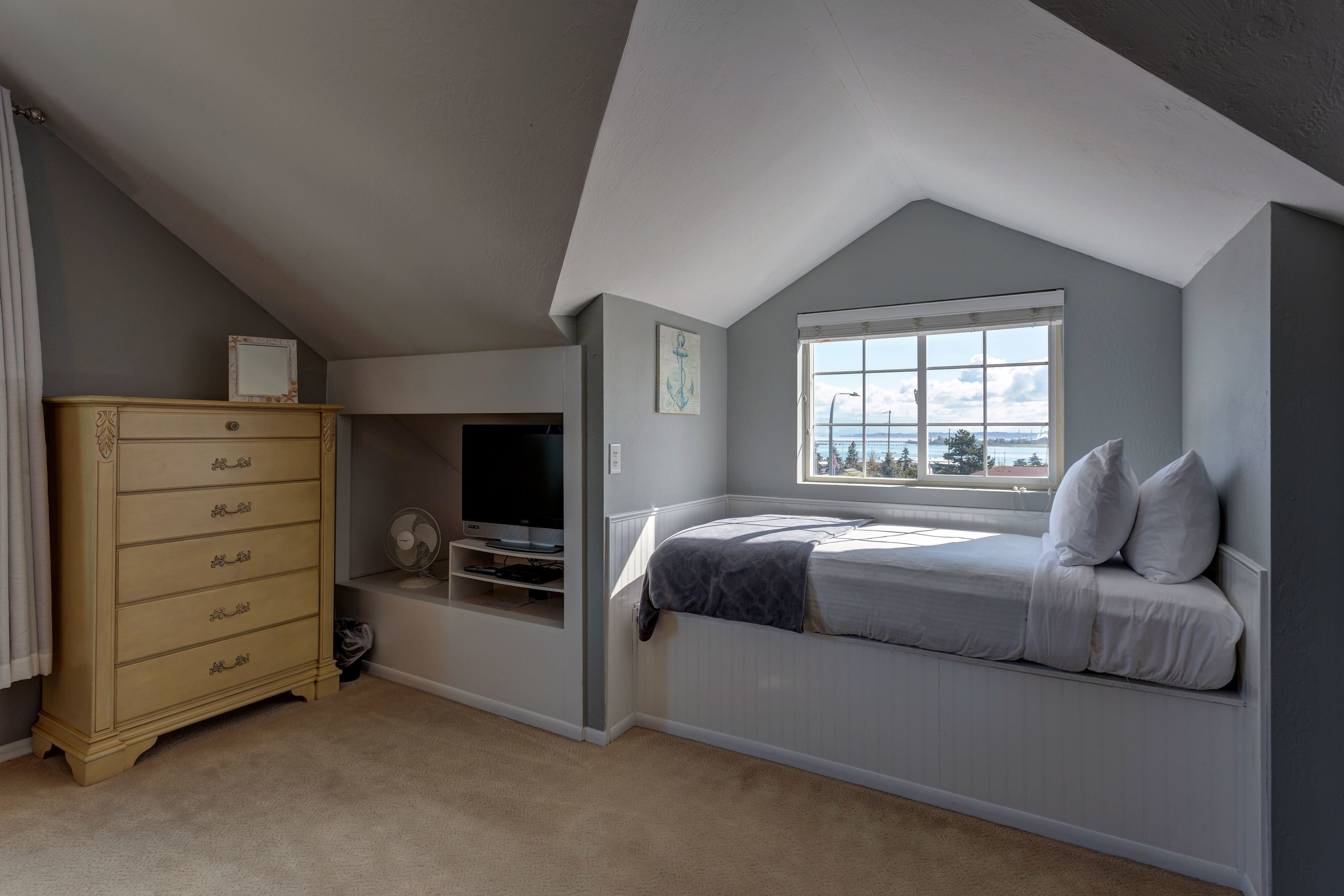 Een slaapkamer met een schuine kap, een inbouwbed, een dressoir en een raam met uitzicht.
