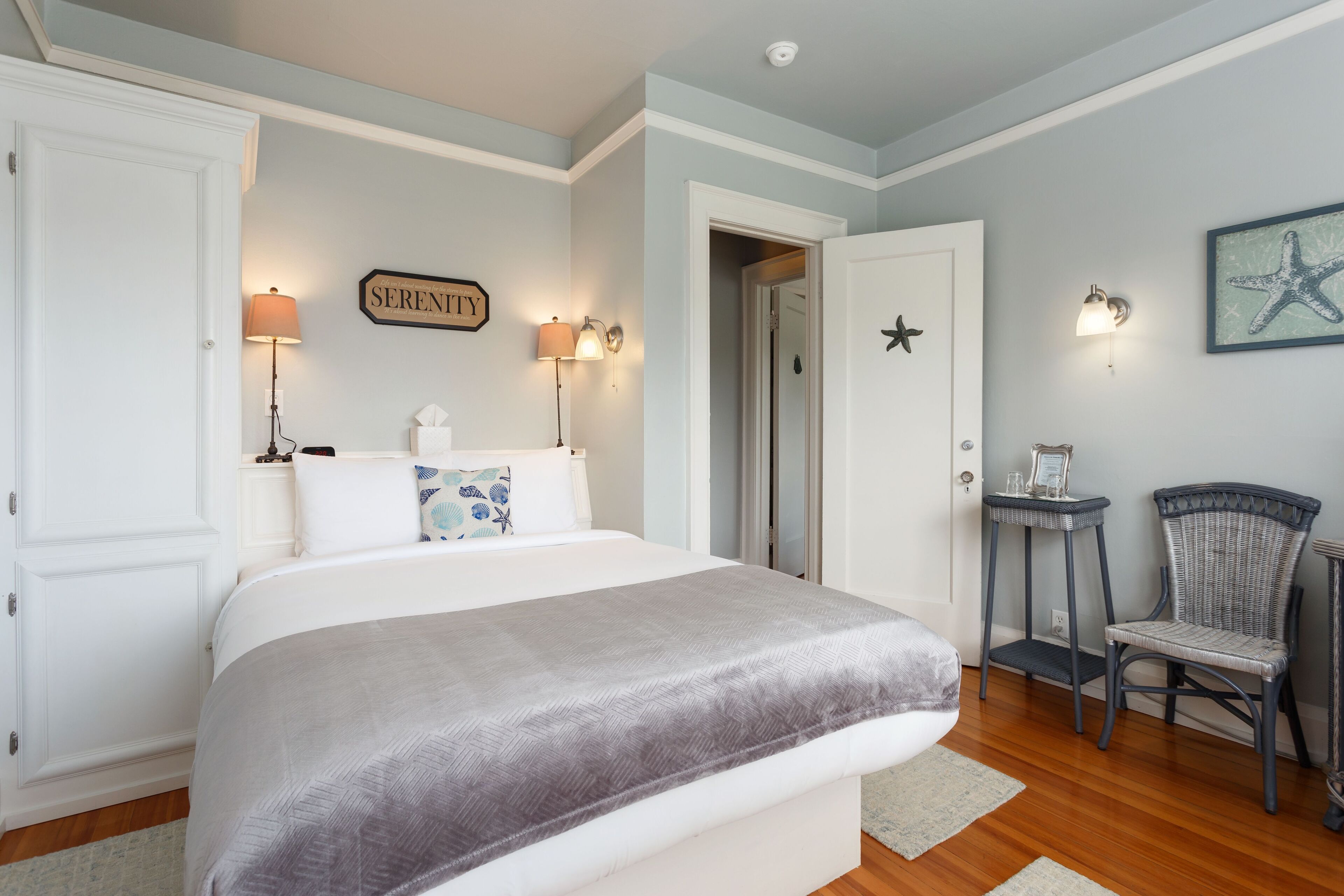 A bedroom with a large bed, two wall-mounted lamps, a chair, and a door leading to another room.