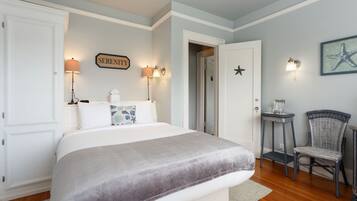 A bedroom with a large bed, two wall-mounted lamps, a chair, and a door leading to another room.