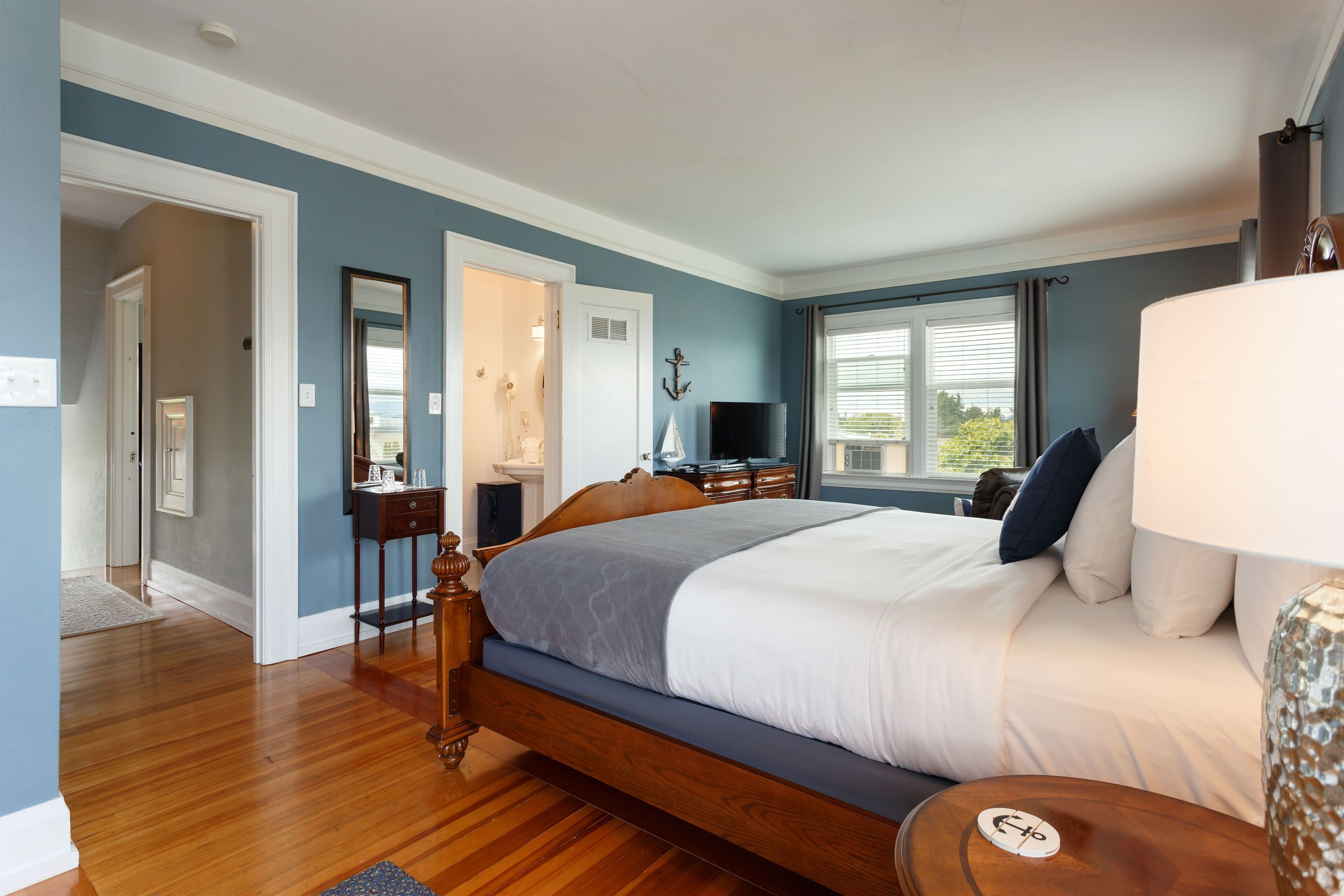 A bedroom with a wooden bed, a nightstand, a dresser, a television, and a window with curtains.