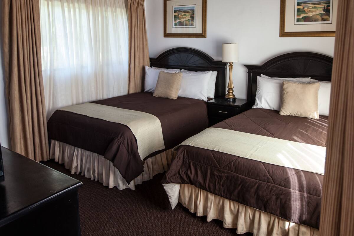 Ein Hotelzimmer mit zwei Betten, einem Nachttisch mit Lampe und zwei gerahmten Bildern an der Wand.