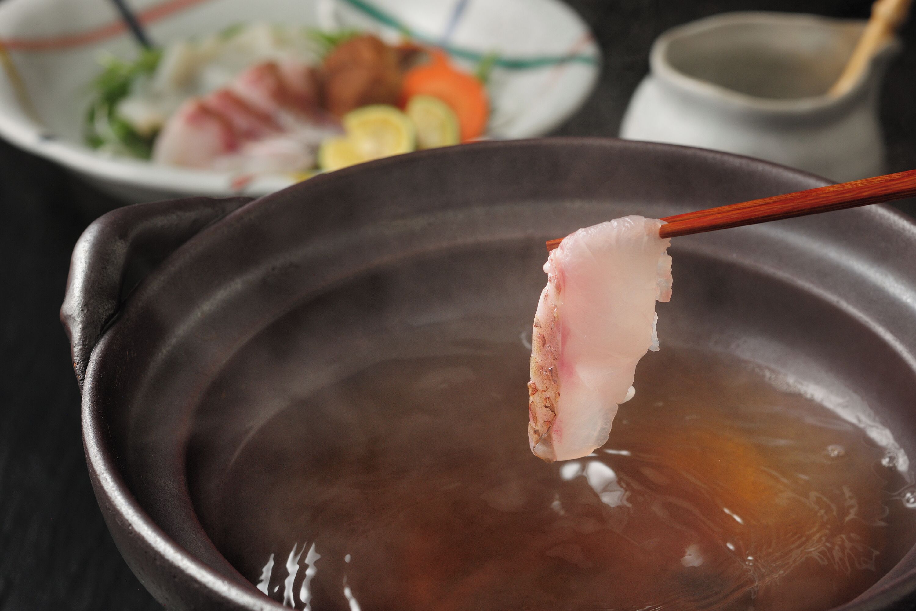 A bowl of soup with chopsticks holding a piece of meat.