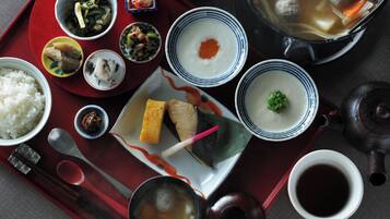 A variety of Japanese dishes including rice, soup, and meatballs, served on a red tray with chopsticks and a teapot.