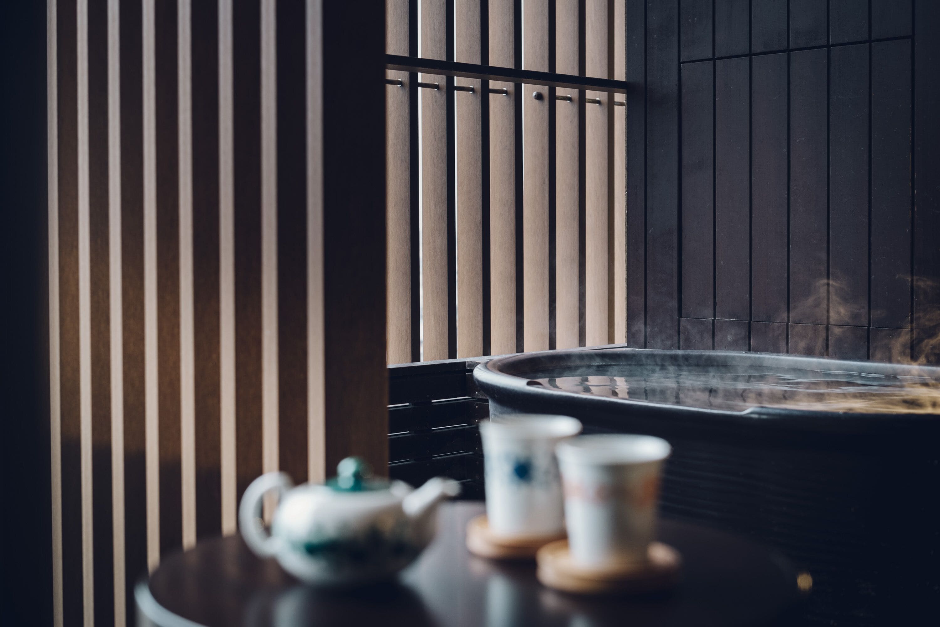 A traditional Japanese-style room with tatami flooring, a low table with a teapot and cups, and a sliding door with vertical slats.