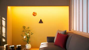 A modern living room with a sofa, a small table with cups, a vase with flowers, and a wall with a geometric decoration.