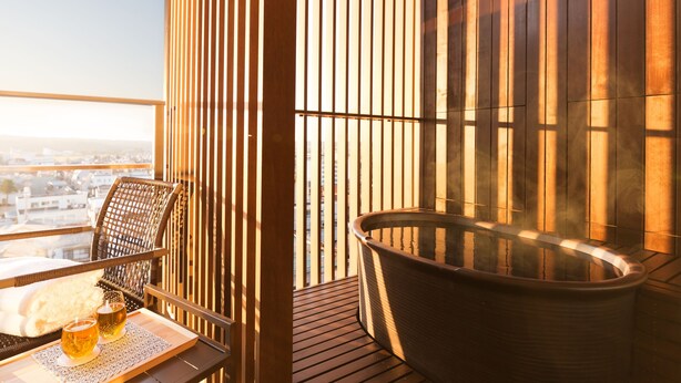 A balcony with a hot tub, a wicker chair, and a table with two glasses of beer. - Hoshino Resorts KAI Kaga (Kaga)