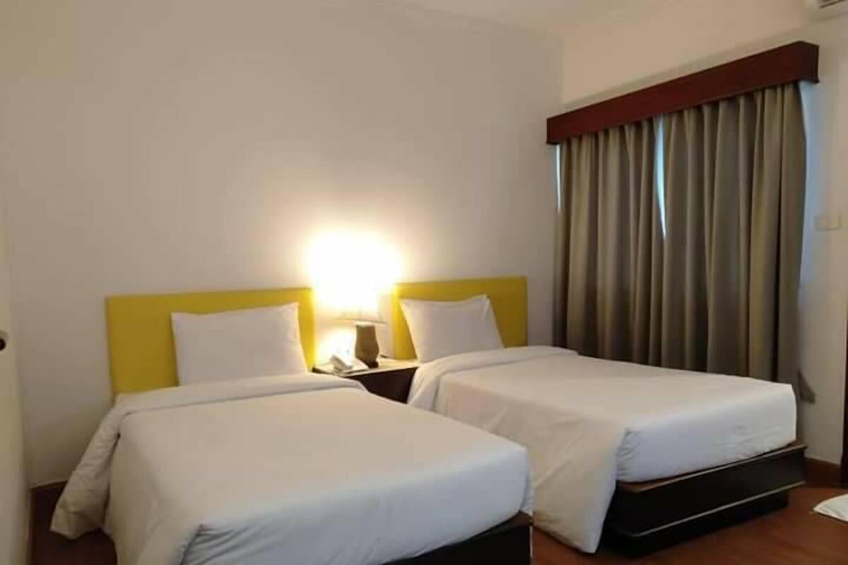 A hotel room with two beds, each with a yellow headboard, white bedding, and a bedside table with a lamp.
