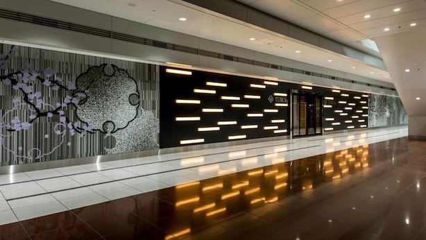 Un vestíbulo moderno con piso reflectante, una pared con arte abstracto y varios paneles iluminados.