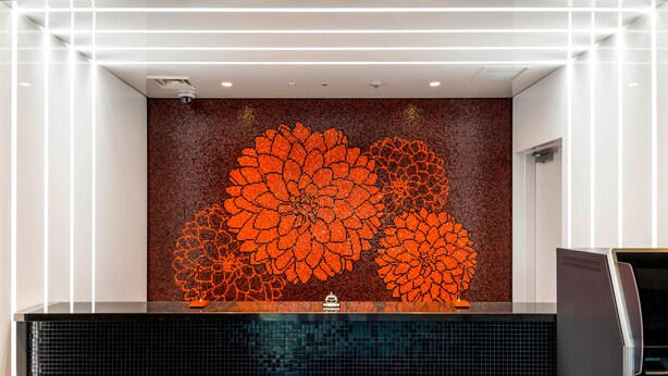 A reception area with a black counter, a large orange floral wall art, and a black tiled backsplash.