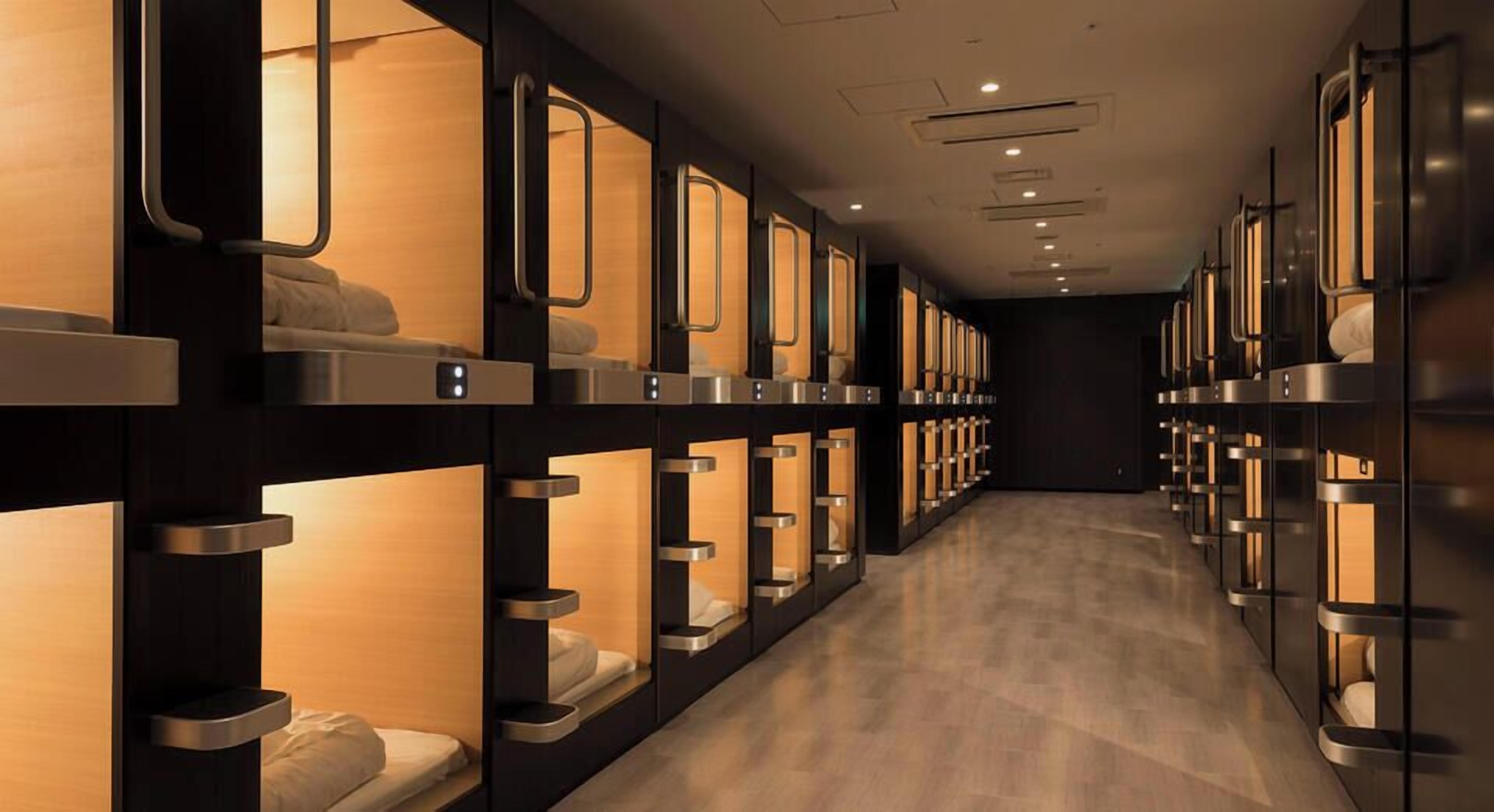 A row of bunk beds with individual lighting, a wooden floor, and a dark wall.