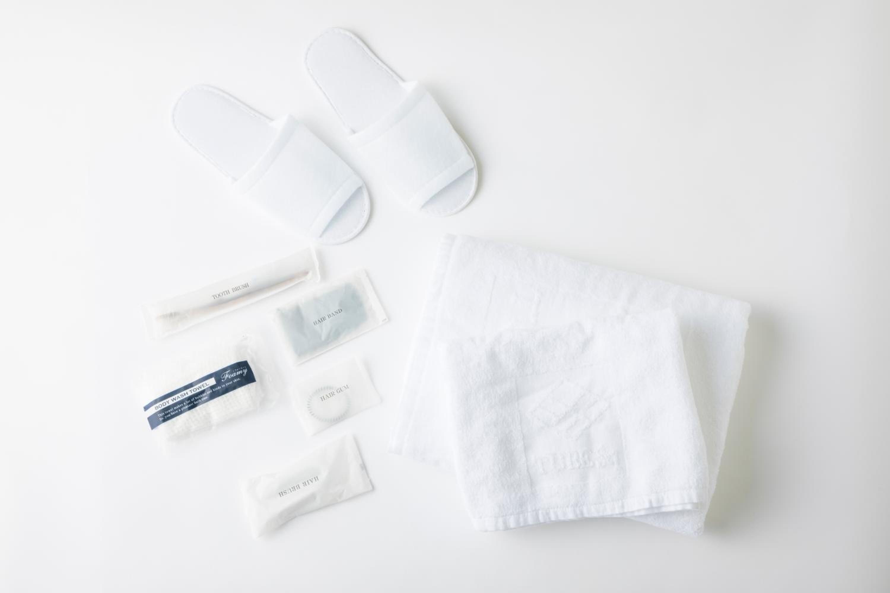 A set of white bath accessories including a body wash towel, hair band, hair gum, and two pairs of white slippers.