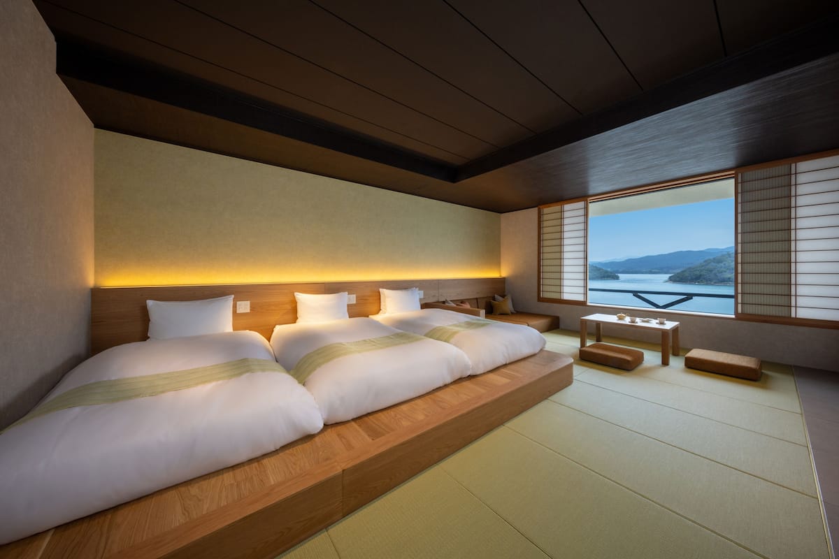 Een moderne hotelkamer met een groot bed, een kleintje tafel en uitzicht op een meer door middel van shoji schermen.
