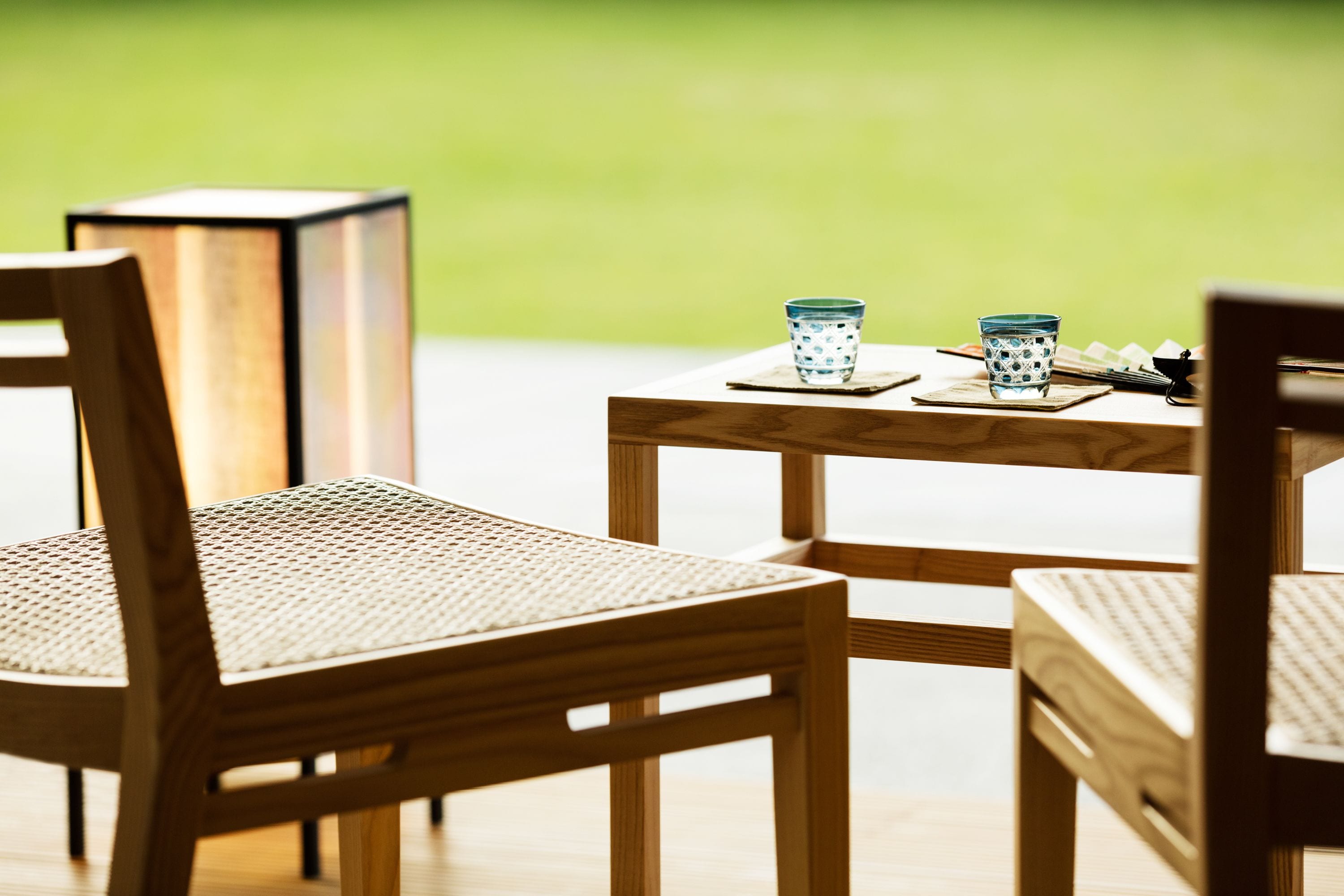 A wooden table with two glass cups and a book, surrounded by wicker chairs.
