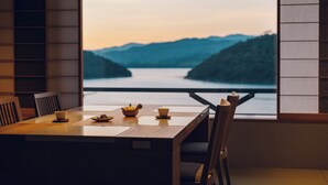 A dining table with chairs, a window with a view of a lake and mountains, and a teapot and cups on the table.