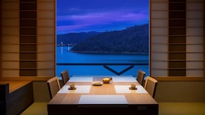 A dining area with a table set for two, a teapot, and a view of a body of water and mountains.