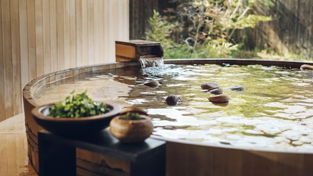 A hot spring bath with a wooden bench and a bowl of green herbs.