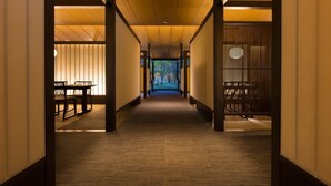 Un corridoio con pavimento in legno e pareti che conduce a una stanza con tatami e un tavolino con sedie.